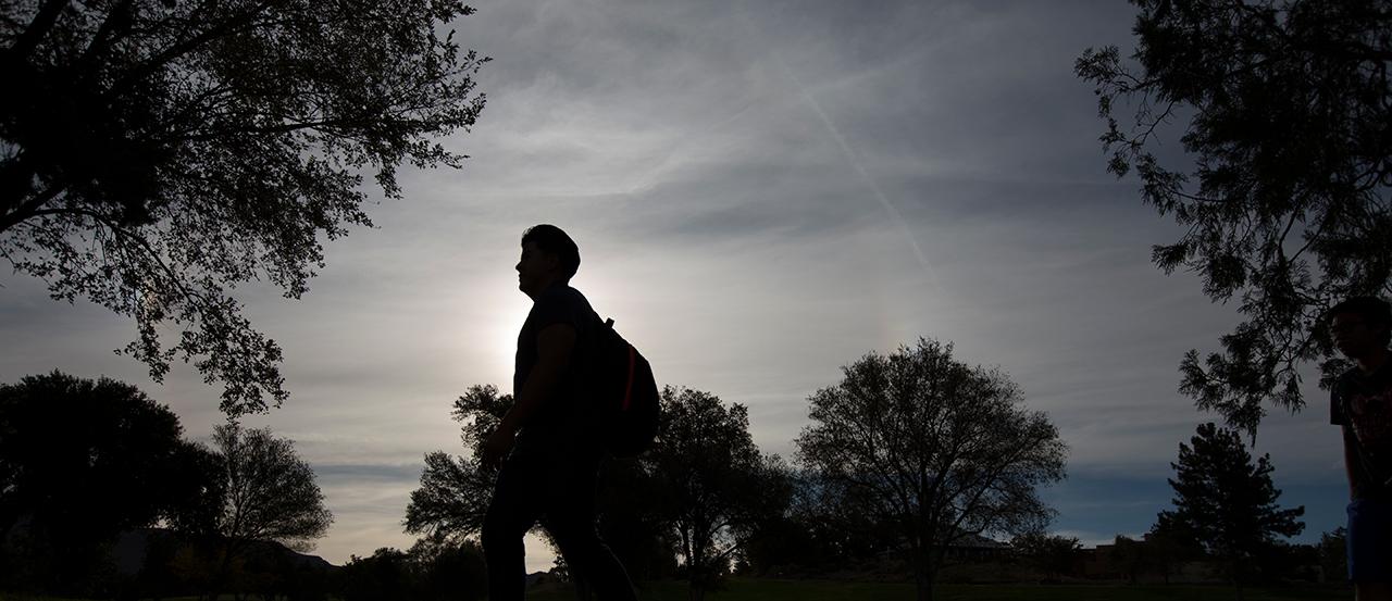 Image of silhouette of a student walking across campus.